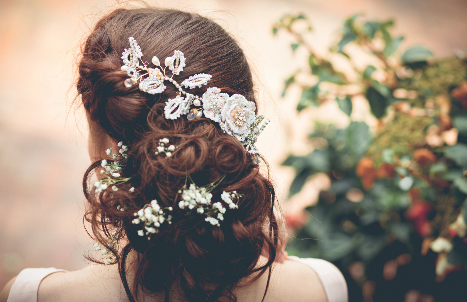behind woman's head of hair flowers and hair jewelry placed throughout it 